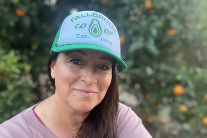 Person wearing a cap with 'Fallbrook Co-op' branding in an outdoor setting with trees and oranges.